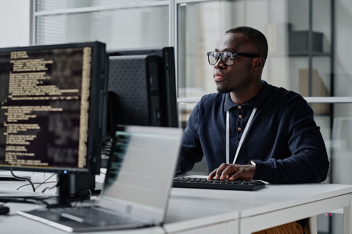 black man with glasses working on a computer with lines of code